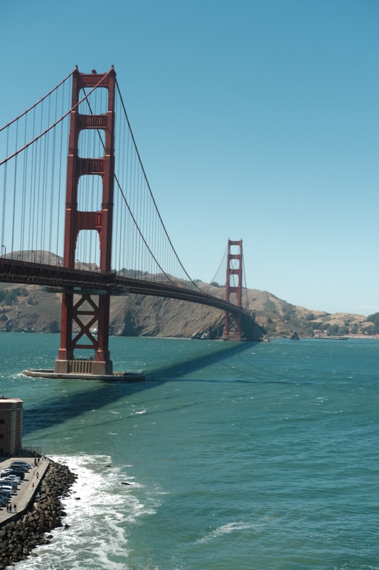 The Golden Gate Bridge crossing blue-green water, with its shadow stretching toward the shoreline.