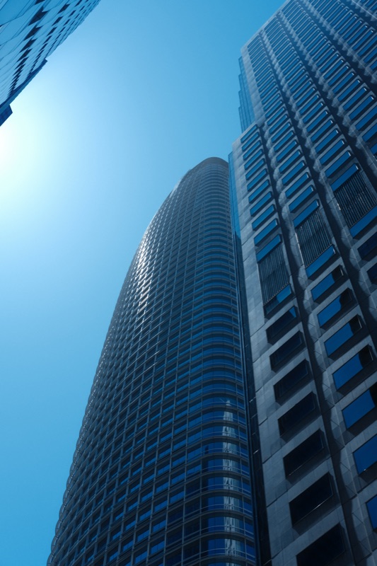 Looking upward between tall buildings into a clear blue sky.