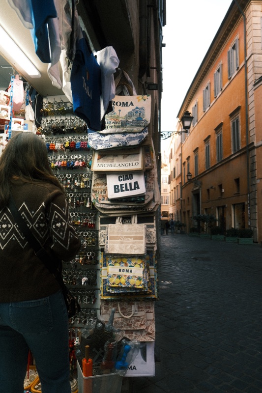 A shopper beside a souvenir stand at the corner of a quiet cobbled street.
