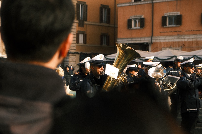 A street band playing brass instruments, glimpsed through the surrounding crowd.